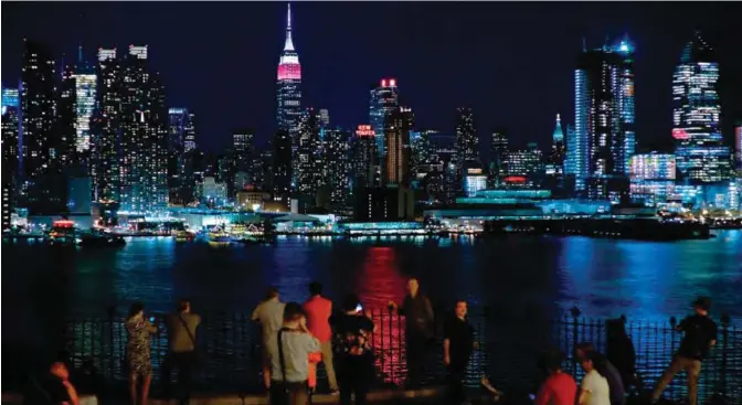  ??  ?? NEW YORK: People look at the New York skyline with the Empire State Building lit in burgundy and white in honor of Qatar Airways and its 10th Anniversar­y of flying to the United States, as seen from Weehawken, New Jersey on June 27, 2017. Qatar's...