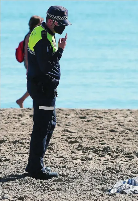  ?? EFE ?? Un policía local recuerda a una mujer que también debe llevar mascarilla en la playa