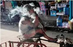  ??  ?? YANGON: A bicycle porter smokes a cigarette as he waits for customers at a wholesale vegetable market in Yangon yesterday. — AFP