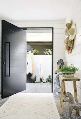  ??  ?? (top right) The bold, black front door is balanced by the gray limestone tiles that anchor the entry.
(right) The herringbon­e-patterned brick paired with some unique found pieces and white paneling makes even this hallway visually stunning.