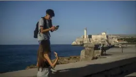  ?? Associated Press ?? A youth uses his smartphone as he and a friend walk along the Malecon seawall in Havana, Cuba, on Nov. 25. Ever-widening access to the internet is offering a new opportunit­y for Cubans looking for hard-to-obtain basic goods.