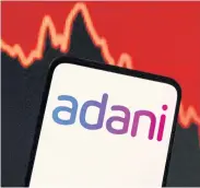  ?? REUTERS ?? The Adani logo is seen on a phone screen against a stock graph in the background.