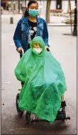  ??  ?? A man wearing a face mask and rain cover is pushed in a wheelchair along a boulevard in Barcelona, Spain on
Wednesday Sept. 9, 2020. (AP)