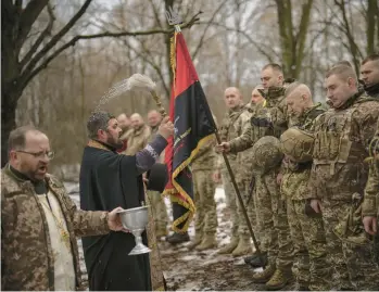  ?? VADIM GHIRDA/AP ?? A priest blesses soldiers with holy water Saturday in Kharkiv, Ukraine, during a ceremony where they were honored for their bravery and accomplish­ments in the war against Russia, now more than a year old.