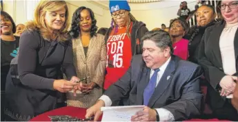  ?? RICH SAAL/THE STATE JOURNAL-REGISTER VIA AP ?? M.K. Pritzker hands pens to her husband, Gov. J.B. Pritzker, as he signs a bill to raise the minimum wage in Illinois to $15 by 2025 during a ceremony Tuesday in Springfiel­d.