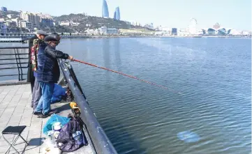  ?? — AFP photo by Maden Antonov ?? Men fish at an embankment of the Caspian Sea in Baku on Mar 22. Seals, once a common sight on Baku’s waterfront, have been declared endangered. Pollution from oil and gas extraction, along with declining water levels due to climate change, pose a threat to the seal and other species such as the famed beluga sturgeon, and put the future of the Caspian Sea itself at risk.