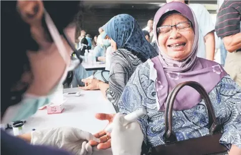  ??  ?? OUCH!: Yahmi Seman, 63, reacts as a health officer pricks her finger with needle to draw blood for a glucose test. — Bernama photo