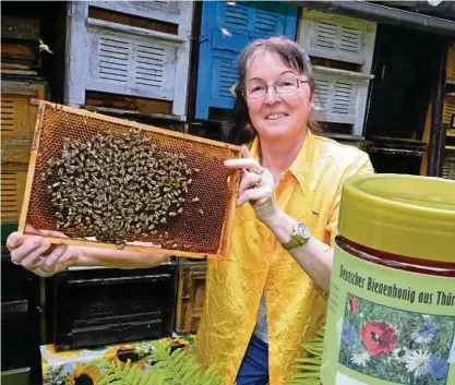  ??  ?? Edith Gebhardt mit einer Wabe, auf der die fleißigen Bienen sind. Rechts Ahornhonig, die die Imkerin abgefüllt hat.