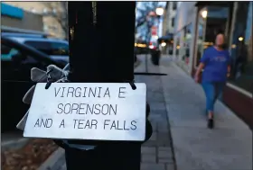  ?? (AP/Martha Irvine) ?? A plaque honoring Virginia “Ginny” Sorenson rests on a lamp post Nov. 3 along Main Street in Waukesha, Wis., as Donna Kalik walks nearby. Sorenson was a leader and member of the Milwaukee Dancing Grannies who was killed when the driver of an SUV sped through a Christmas parade in Waukesha last November, killing six and injuring dozens of other people.