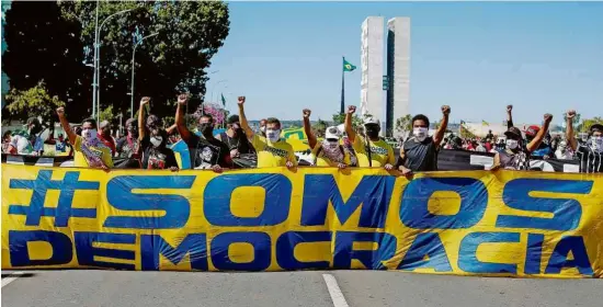  ?? Sergio Lima - 21.jun.20/AFP ?? Manifestan­tes com faixa pró-democracia em ato contra o presidente Jair Bolsonaro, em Brasília