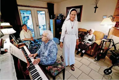  ??  ?? Sister Maria Faulkner walks through the living room of the Gospel of Life Dwelling as Annabelle Miller plays piano.