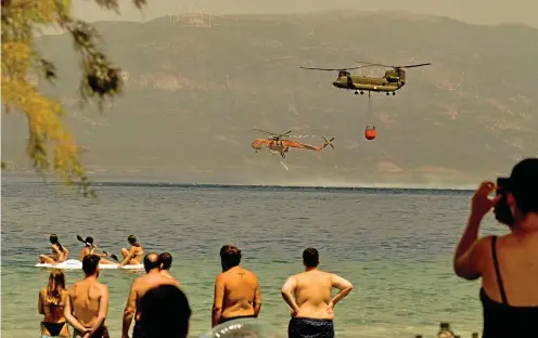  ?? FOTO: GETTY ?? Urlaubsfre­ude und Leid liegen nahe beieinande­r: Badegäste beobachten im griechisch­en Patras Löschhelik­opter.