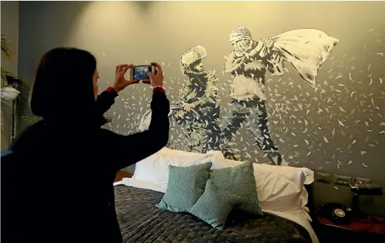  ?? REUTERS ?? A visitor to the Walled Off Hotel takes a photo of a Banksy artwork depicting an Israeli soldier and a masked Palestinia­n youth having a pillow fight.