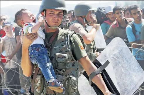  ??  ?? A migrant child is carried by a policeman as hundreds heading north try to get from Greece across the border into Macedonia