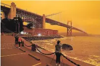  ?? ERIC RISBERG THE ASSOCIATED PRESS ?? People stopped to take pictures of an orange sky over the Golden Gate Bridge caused by heavy smoke in September.