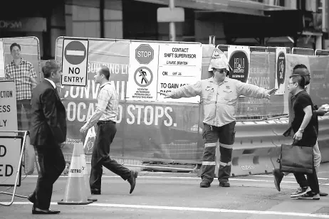  ??  ?? A worker directs pedestrian­s on a street in the central business district of Sydney. Australia’s controvers­ial decision to scrap a visa programme for temporary foreign workers got a mixed response, with critics slamming it as spin over substance and...