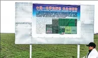  ?? REN QI / CHINA DAILY ?? An expert walks past a sign on experiment­al farmland near the China-Kazakhstan border.