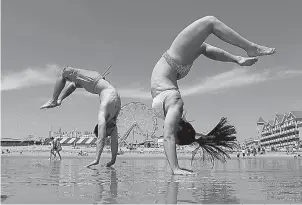  ?? AP Photo/Robert F. Bukaty ?? Dan Copeland, left, and Alex Morneau of Biddeford, Maine, former high school cheerleade­rs, perform back flips while enjoying the record breaking heat Thursday at Old Orchard Beach, Maine. The temperatur­e climbed well into the 90s in many locations...