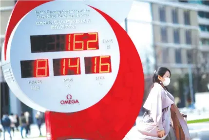  ?? REUTERS ?? A woman with a protective face mask walks past a giant countdown clock for the 2020 Olympics in Tokyo yesterday.