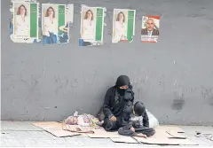  ?? AFP ?? A beggar and her children sit on the sidewalk beneath electoral posters in the Lebanese capital Beirut. Parliament­ary polls will be held on Sunday.