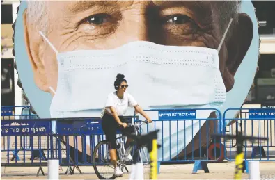  ?? NIR ELIAS / REUTERS ?? A cyclist passes a sculpture decorated with images of people wearing protective masks at Habima Square. Leading rabbis and ultraortho­dox political leaders have been encouragin­g Israeli communitie­s to ignore health directives.