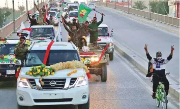  ?? AFP ?? Above: Members of the Hashed Shaabi (Popular Mobilisati­on) paramilita­ry forces flash the victory sign as they wave flags of the organisati­on and its groups while parading in the streets of Karbala on Monday.