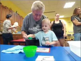  ?? ZACHARY SRNIS — THE MORNING JOURNAL ?? Donna Baron helps her grandson Broody Sowders, both North Ridgeville residents, with an experiment using water and magnets Sept. 4 at the Lorain Public Library System North Ridgeville branch.