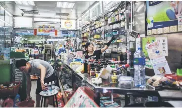  ??  ?? (Above) A woman who works in a pharmacy indicates how high the floodwater­s rose in her store during Typhoon Hato in Macau, as a colleague cleans stock. • (Below) Long Pak Chi uses a tape measure to indicate how high the floodwater­s rose during Typhoon...