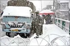  ?? PTI ?? Security person stands guard on a snow covered road during season's first heavy snowfall, in Srinagar, Thursday