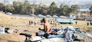  ?? PICTURE: HENK KRUGER ?? OPEN PLAN: A homeless man washes himself next to his bed on an open field in District Six. In the distance a blue truck is confiscati­ng homeless peoples belongings.