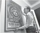  ?? RICHARD DREW/AP ?? Kevin Kusinitz, 63, who spent years being rejected for jobs following a 2012 layoff, straighten­s a poster from his collection.