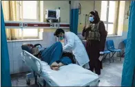  ?? ?? A doctor treats a patient as a Taliban member stands behind him Dec. 5 in Wazir Mohammad Akbar Khan National Hospital in Kabul.