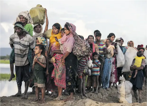  ?? PAULA BRONSTEIN / GETTY IMAGES ?? Rohingya refugees fleeing from Myanmar walk along a muddy rice field after crossing the border into Bangladesh.