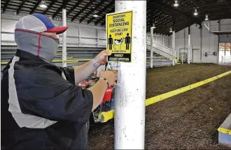  ?? BILL LACKEY / STAFF ?? Brad Spencer hangs signs in the barns at the Clark County Fairground­s on Thursday reminding fairgoers to social distance.