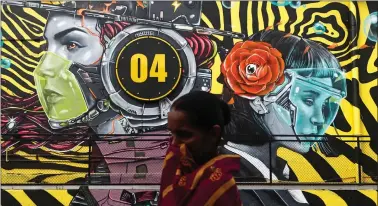  ?? REUTERS ?? A woman walks past a graffiti of people wearing protective masks amidst the spread of the coronaviru­s disease, on the outskirts of Mumbai, on Wednesday.