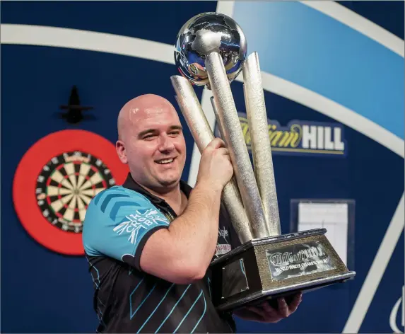 ?? Photo by TOLGA AKMEN/AFP/Getty Images ?? Rob Cross holds aloft the winner’s trophy after beating Phil Taylor during the PDC World Darts Championsh­ip 2018 final game in London on Monday. Debutant Cross stunned 16-time world champion Phil Taylor in the final after beating him 7-2.