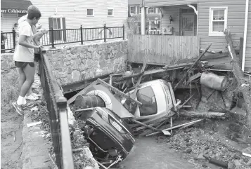  ?? David McFadden/Associated Press ?? ■ Residents gather by a bridge Monday to look at cars left crumpled in one of the tributarie­s of the Patapsco River that burst its banks as it channeled through historic Main Street in Ellicott City, Md. Sunday’s destructiv­e flooding left the former...