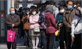  ?? (AP/Andy Wong) ?? A man wearing a face mask to help protect from the coronaviru­s walks Thursday by masked residents who wait in a line to get their throat swabbed at a private mobile coronaviru­s testing facility near residentia­l buildings in Beijing.