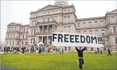  ?? Paul Sancya The Associated Press ?? A protester carries a sign at a rally Thursday against Michigan’s coronaviru­s stay-at-home order at the State Capitol in Lansing, Mich.