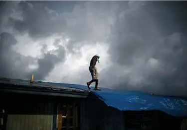  ?? RAMON ESPINOSA — THE ASSOCIATED PRESS ?? Trevon Laing walks the roof of his house to repair the damage made by Hurricane Dorian, in Gold Rock Creek, Grand Bahama, Bahamas, Thursday. Trevor says “After the hurricane they had me for dead, My momma was crying.” When he returned, he said he found his brother crying on the front porch.”I’m like, ‘Hey, I’m not dead! You guys have no faith in me. I’m a survivor,’” he said, adding with a laugh, “He was shocked and mad at the same time.”