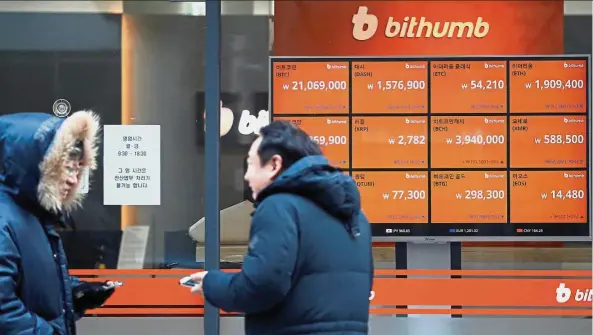  ?? Reuters ?? Trading halt soon:
People walk past an electric board showing exchange rates of various cryptocurr­encies at Bithumb cryptocurr­encies exchange in Seoul. The South Korean government is preparing a bill to ban trading of the virtual currency on domestic...