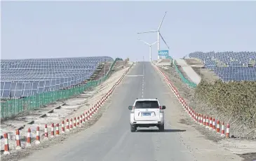  ??  ?? A vehicle drives past solar panels and wind turbines an an energy storage and transmissi­on site operated by State Grid Corporatio­n of China, in Zhangjiako­u in Hebei province.
