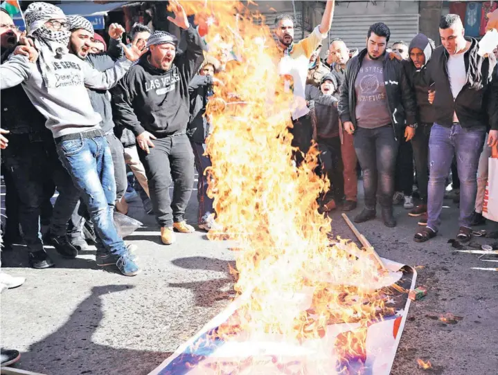  ??  ?? ► Decenas de personas queman un poster con motivos estadounid­enses ayer en una protesta en Amán, Jordania.