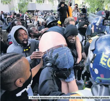  ??  ?? > Patrick Hutchinson carries an injured man away during Saturday’s protests