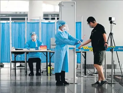  ?? STR / AFP ?? Una empleada del aeropuerto internacio­nal de Pekín toma la temperatur­a a un pasajero
