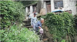  ?? FU TING/AP ?? Lin Fazhen, 60, left, leaves his home with a neighbor in the former fishing village of Houtouwan. They are two of only five residents left from the 3,000 that once lived in the village.