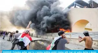  ?? — AFP ?? BAGHDAD: Protesters gather next to a burning building amidst clashes with Iraqi riot police during a demonstrat­ion against state corruption and poor services yesterday.