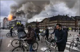  ?? EMIL NICOLAI HELMS — RITZAU SCANPIX VIA AP ?? People ride bicycles as smoke rises from the Old Stock Exchange in Copenhagen, Denmark, Tuesday.