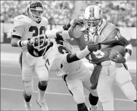  ?? (AP file photo) ?? SMU running back Eric Dickerson (right) pushes his way past Arkansas’ Nathan Jones (center) in a 1982 matchup that finished in a 17-17 tie. A 40-yard pass interferen­ce penalty against Jones set up the game-tying touchdown for the Mustangs. In 1984, the NCAA rules committee made pass interferen­ce a 15-yard penalty rather than a spot of the foul call.