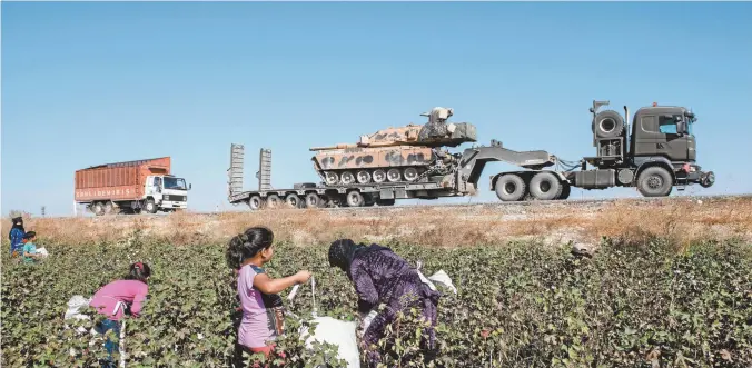  ??  ?? Turkish military vehicles carrying tanks and equipment head to the Syrian border as farmers work in a cotton field.
